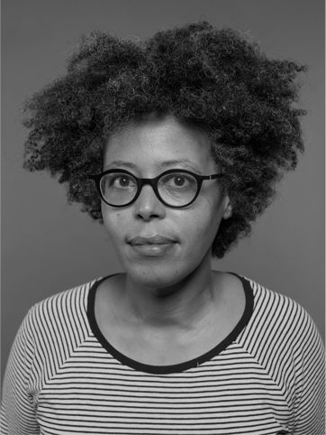 Portrait en noir et blanc de Sahar. Sahar porte un pull à rayure, des lunettes à monture foncée et a les cheveux courts bouclés.