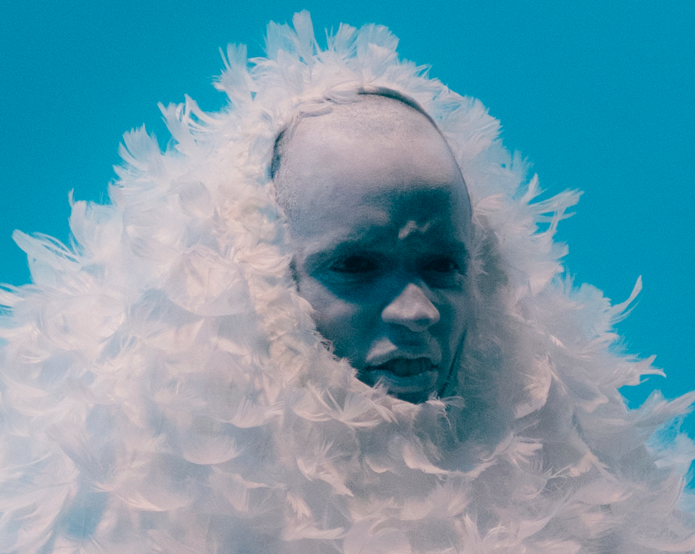 Marvin est sur n fond bleu, il grimace comme s'il était en colère. Visage grimé en blanc et son costume de plumes blanches qui ne laisse qu'apercevoir son visage grimacé.