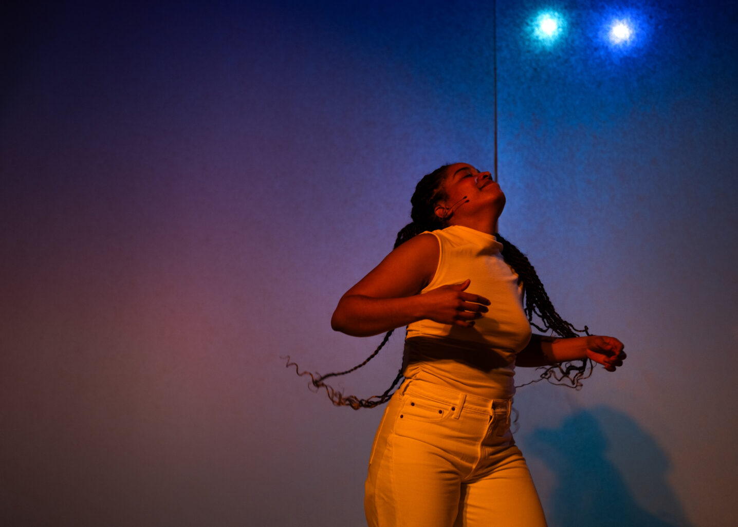 Elle, danse. Elle est éclairée par une lumière orangée dans un fond bleuté.
