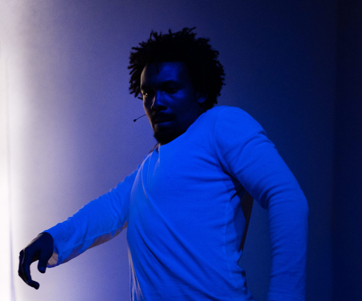 Lui, danse et est dans une position comme affolé. Il est éclairé par une lumière bleue.