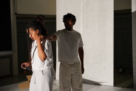 Sur la photo, on voit les deux protagonistes, Mélissa qui joue ELLE et Uchenna qui joue LUI. Ils sont habillés en blanc, LUI est dans l'ombre, derrière ELLE, une main sur l'épaule d'ELLE qui tient la main sur son épaule et regarde vers le bas.